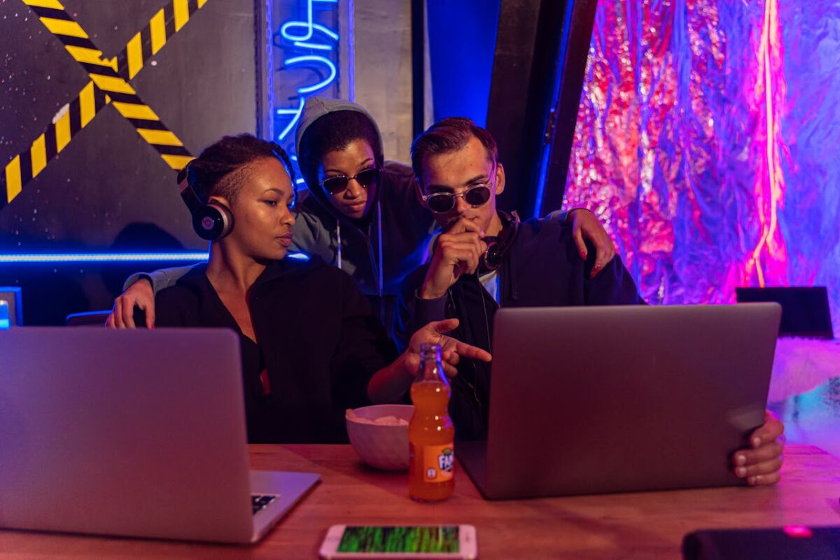 Attractiv Movies Three people collaborate on laptops in a cyber-themed workspace, discussing strategies.