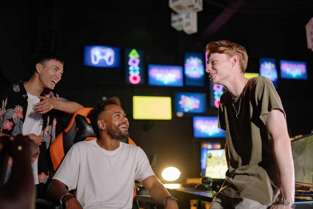 Three young men laughing and enjoying a gaming session in a vibrant room with multiple screens.
